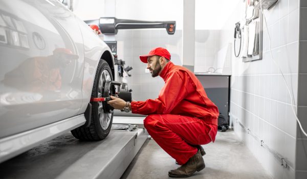 Handsome auto mechanic in red uniform fixing disk for wheel alignment at the car service